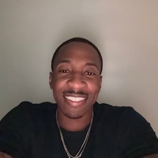 Smiling Black man with a mustache wearing a black shirt and silver chain necklace.